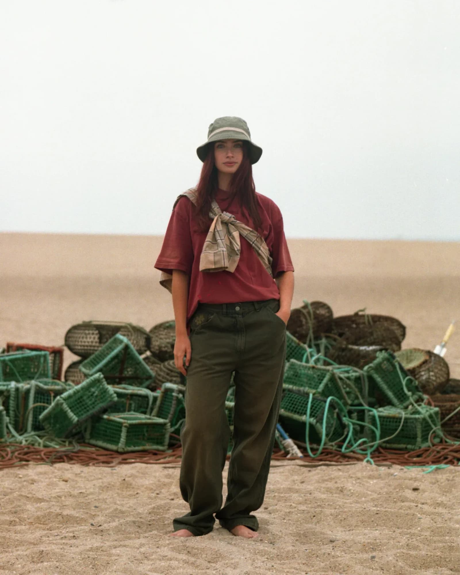 Model on beach beside stacked lobster traps