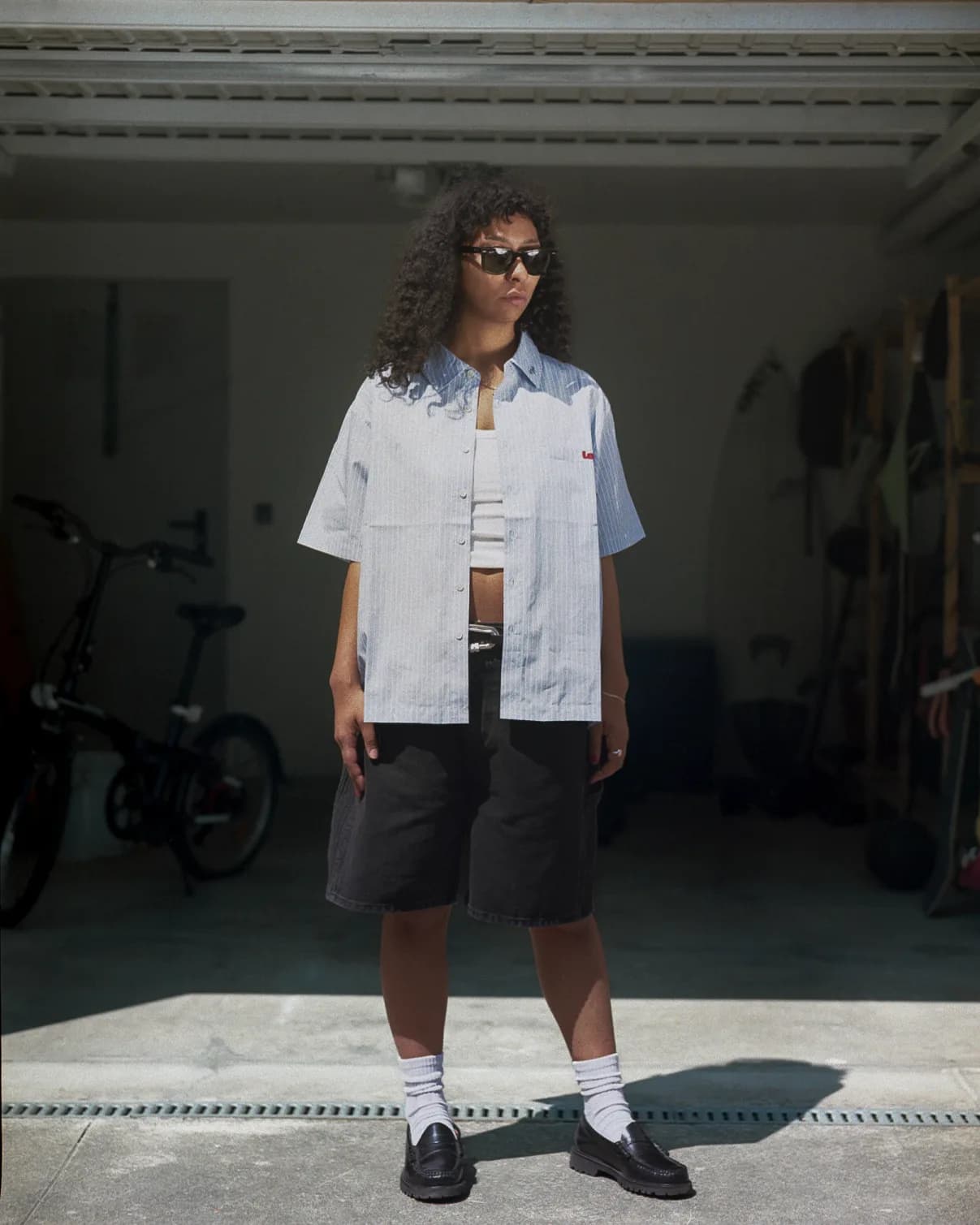 Woman in white pinstripe shirt and black shorts, garage doorway